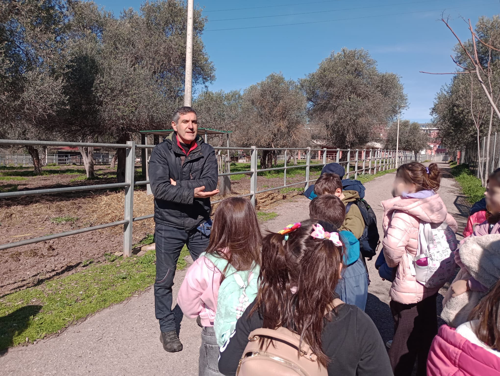 Bambini della scuola primaria in visita al Dipartimento di Medicina Veterinaria di Sassari mentre ascoltano la spiegazione di un docente negli spazi esterni tra i recinti degli animali
