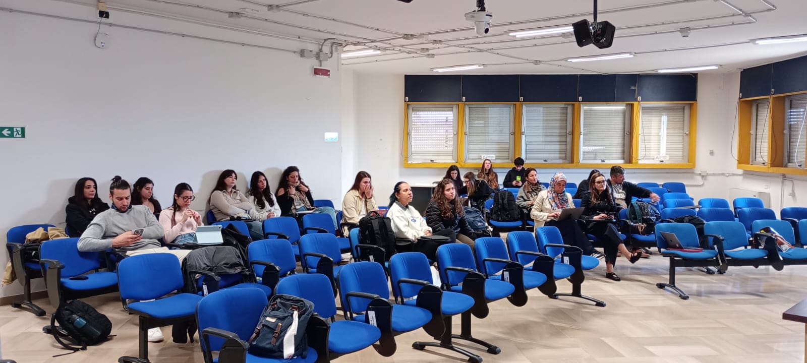 Partecipanti seduti in aula universitaria durante un seminario, con pubblico composto da studenti e docenti in ascolto