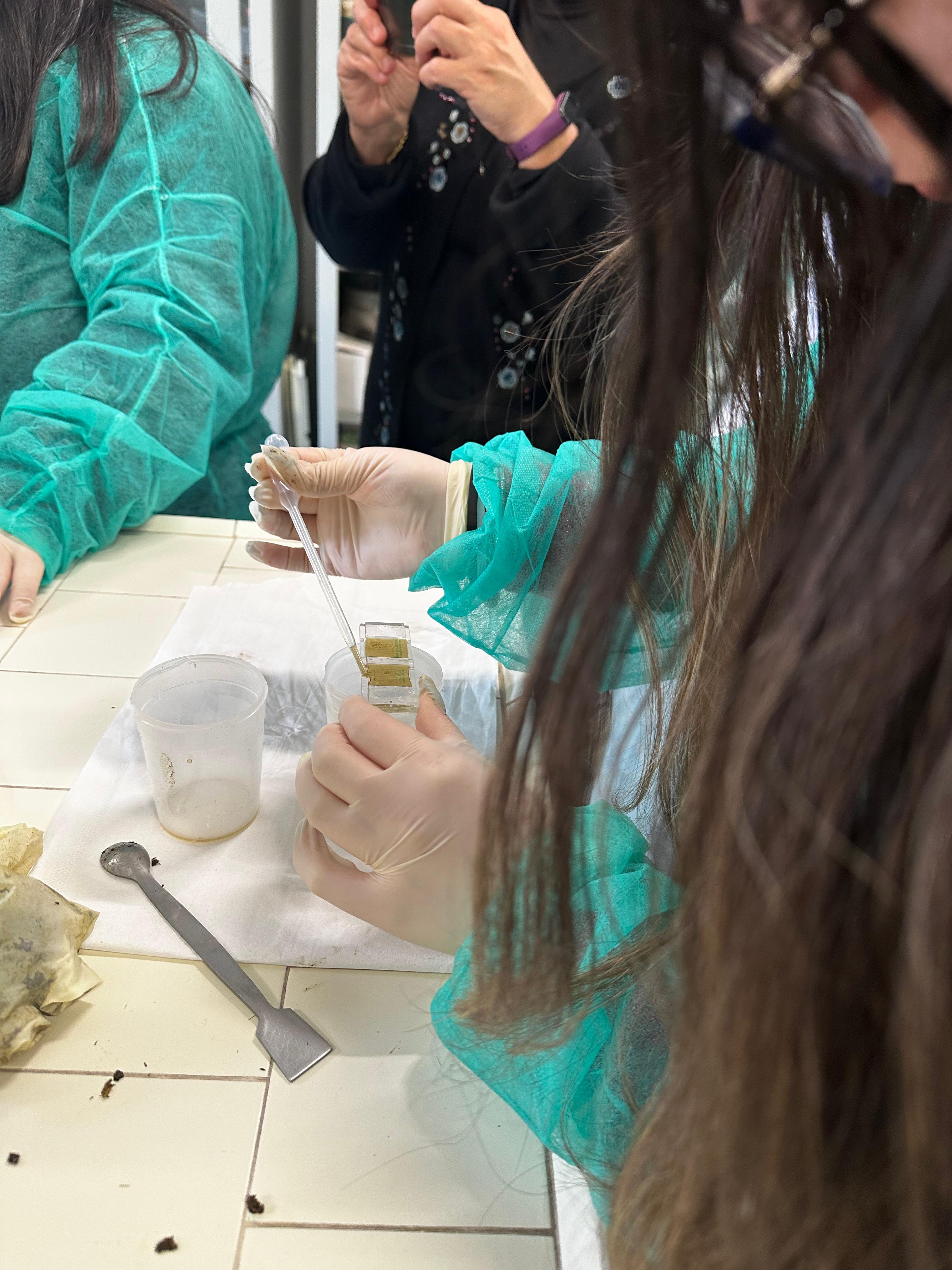 Primo piano di una studentessa durante un’attività di laboratorio mentre deposita con una pipetta un campione su alcuni vetrini.
