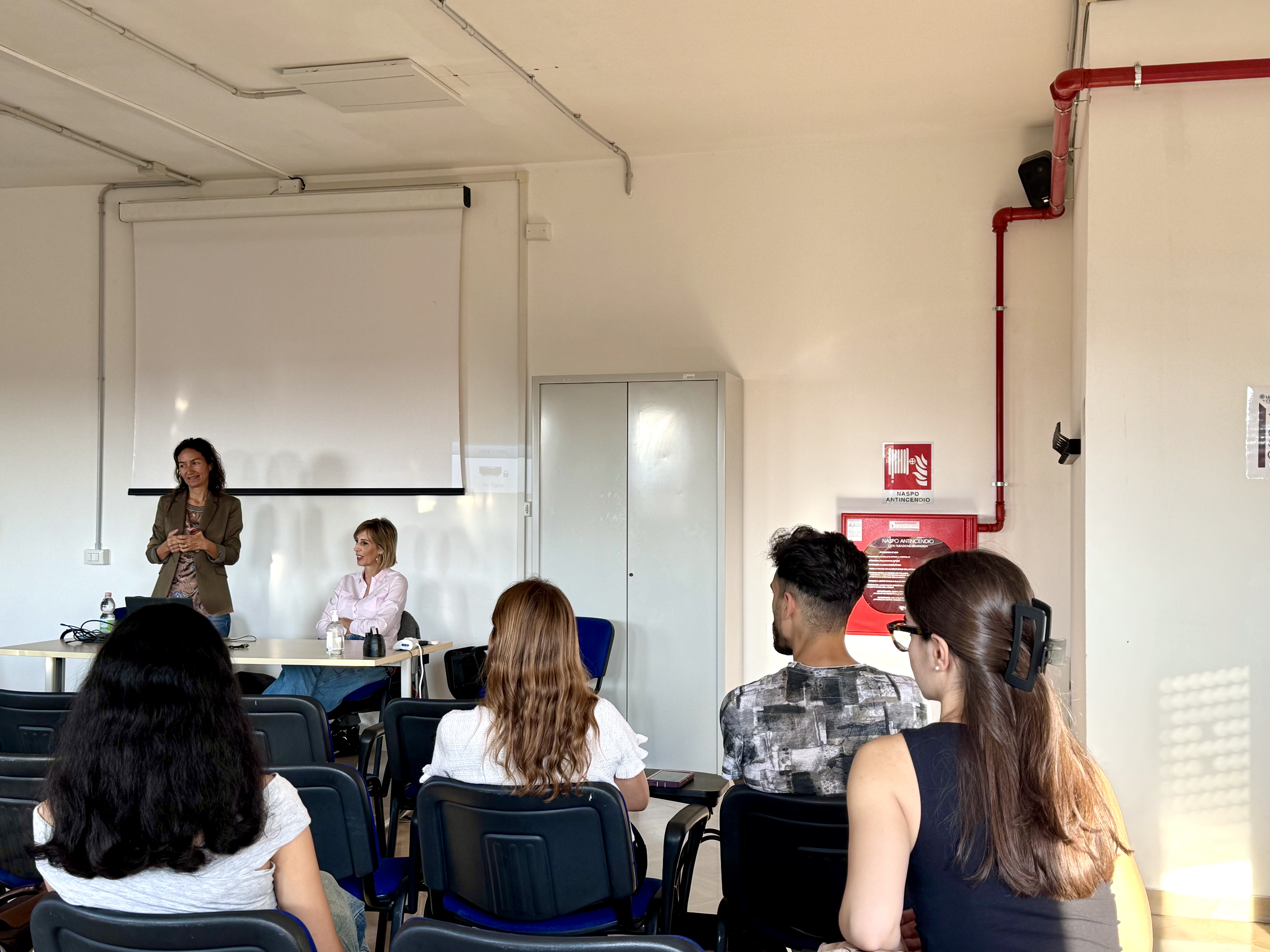 Studentesse e studenti ascoltano la docente in piedi accanto alla cattedra durante il Welcome Day di Biotechnology for Human and Animal Health.