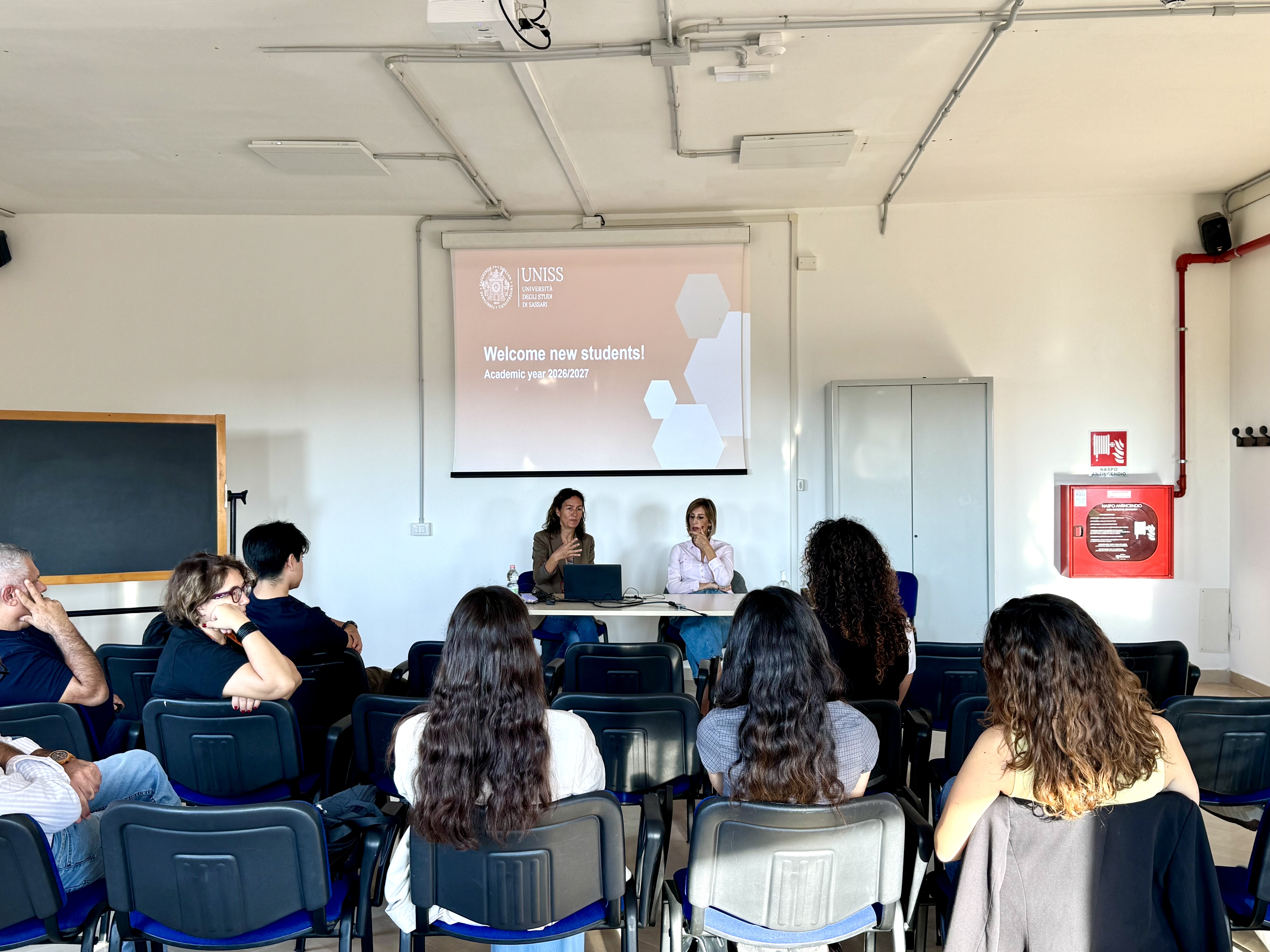 Due relatrici alla cattedra incontrano le studentesse e gli studenti di Biotechnology for Human and Animal Health, sotto la slide di benvenuto dell’Università di Sassari.
